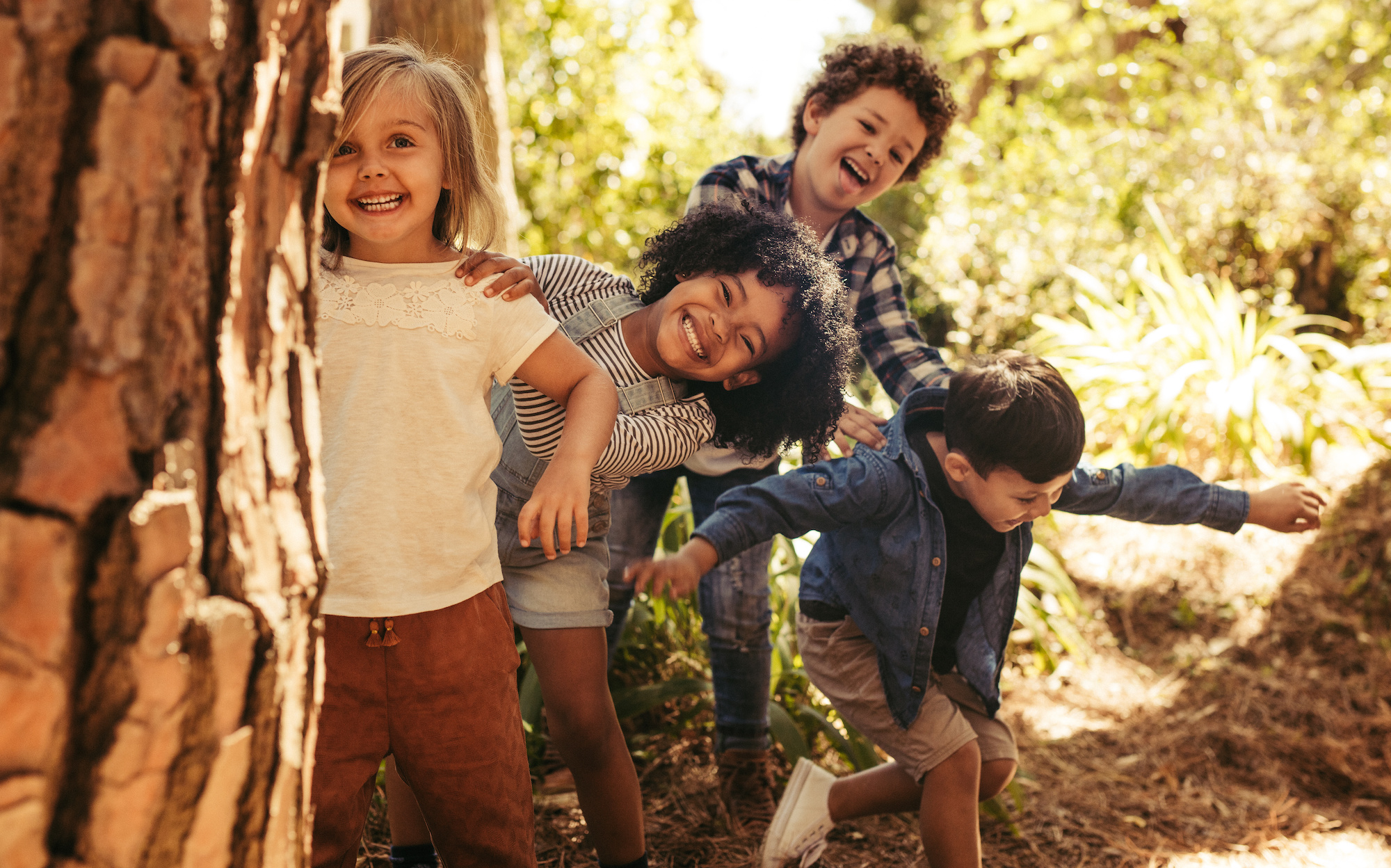 Vier Kinder im Wald hinter einem Baum, Kieferorthopädie an der Parkinsel, Ludwigshafen